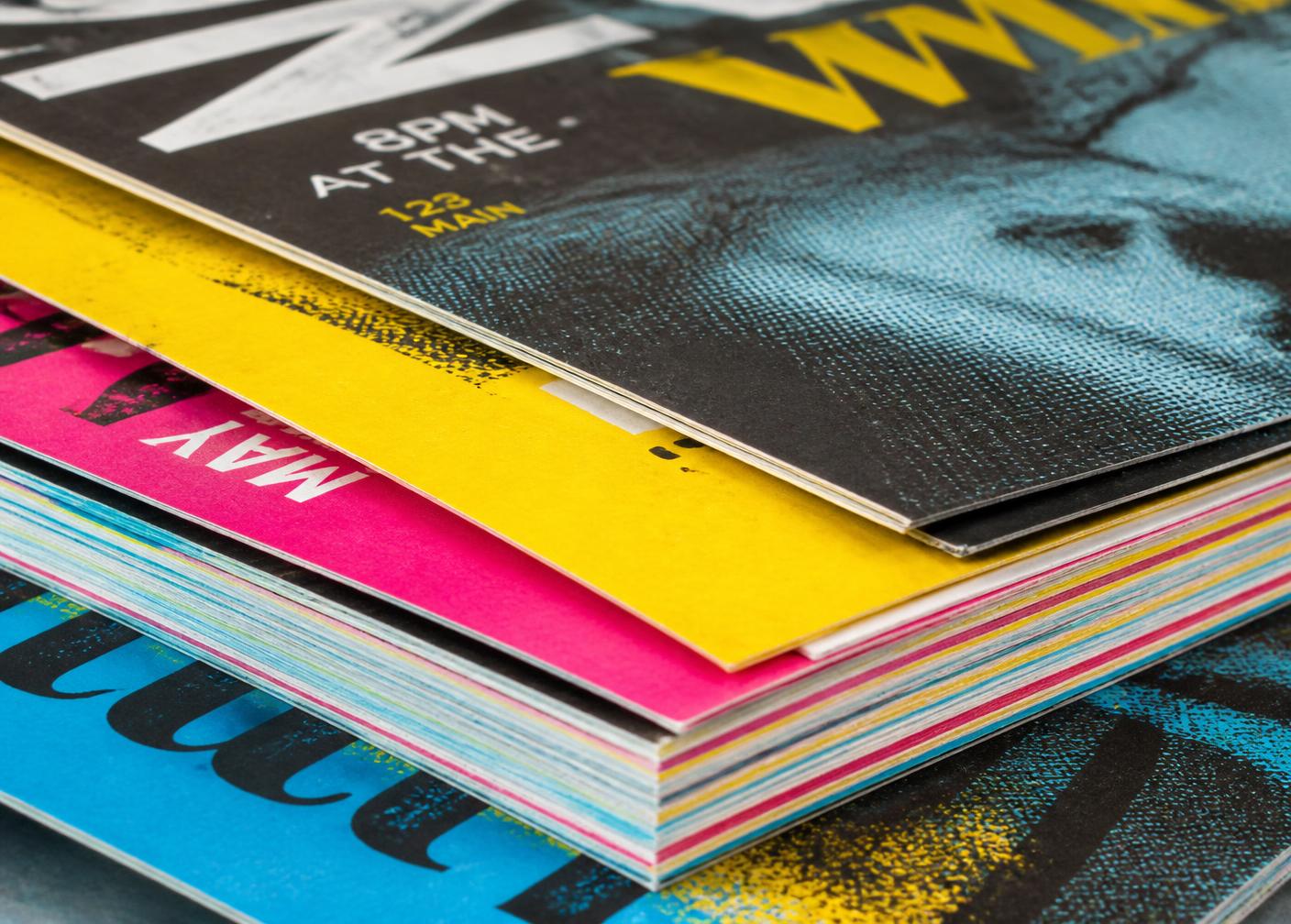 Stack of freshly printed brochures in cyan, magenta, and yellow bleeds